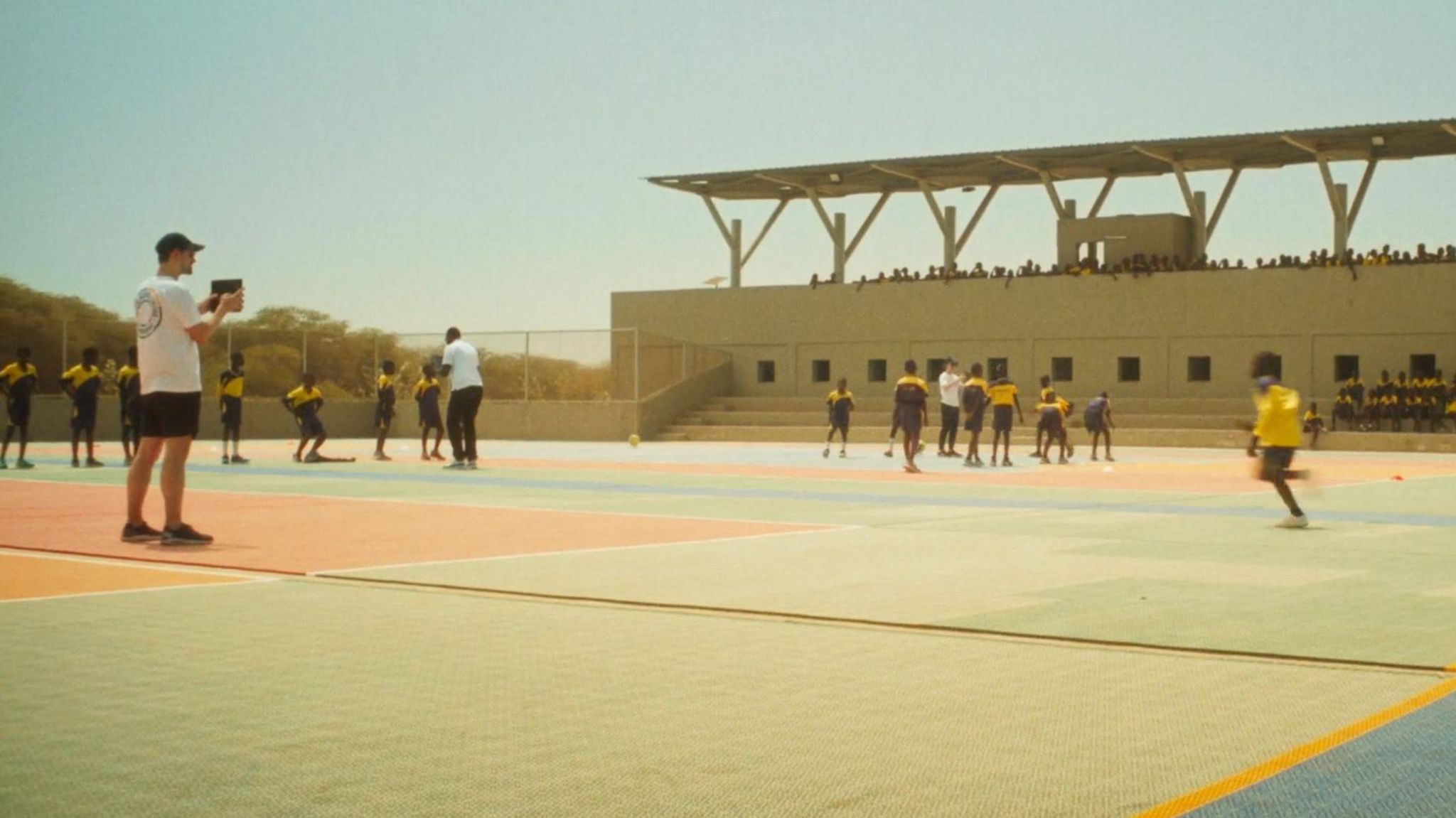 A man holds a tablet up and film a boy running across a square