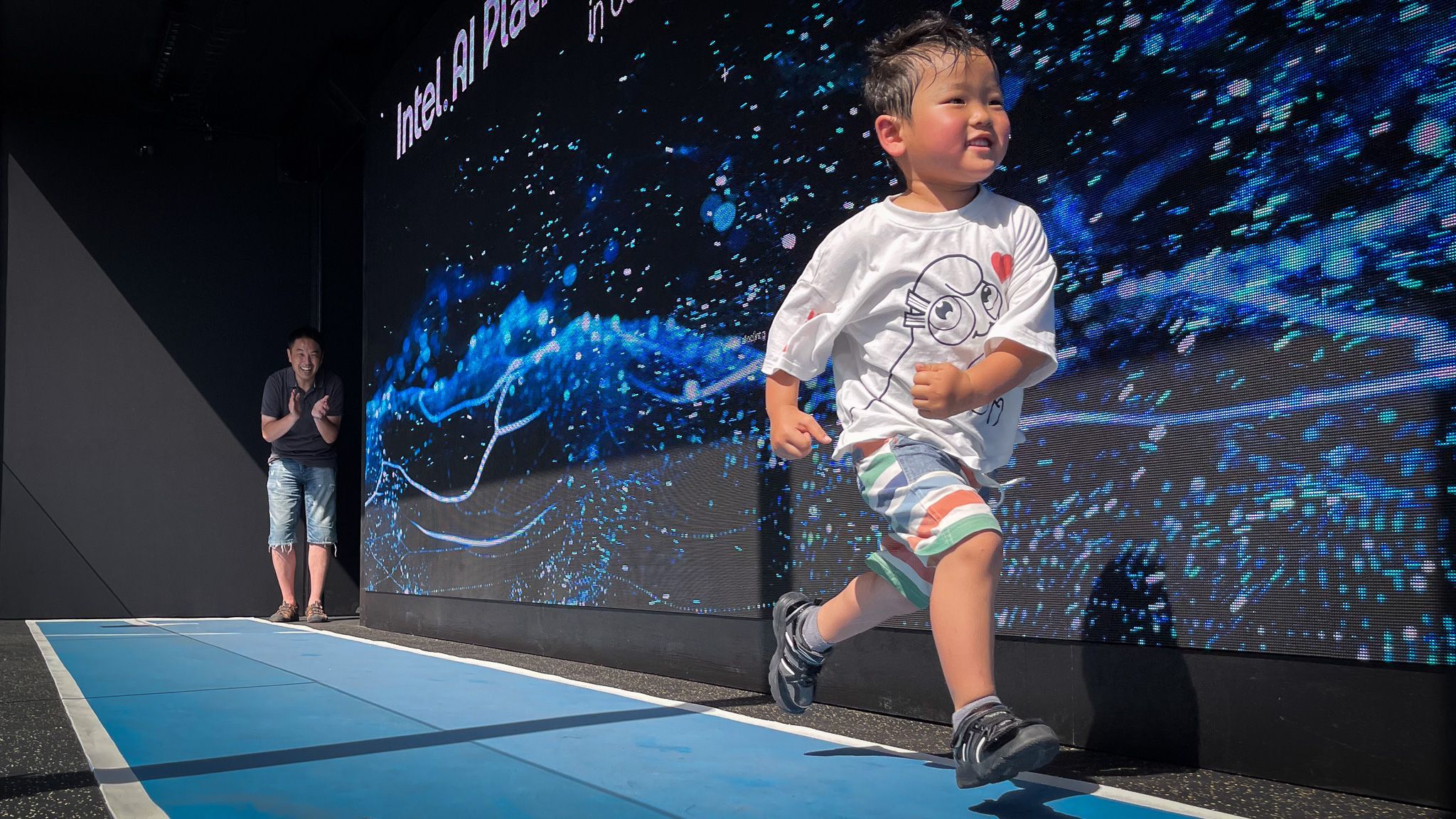 A young boy sprints down a track while his father watches