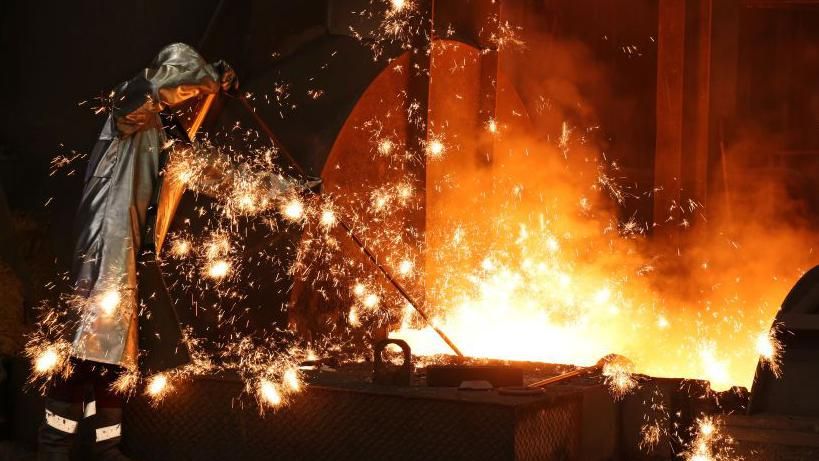 Sparks fly as a worker takes a sample of molten iron flowing from a blast furnace in Duisburg, Germany