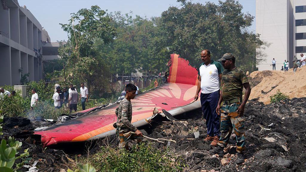 Men inspecting aircraft debris at the crash site of Air India flight AI171 in Ahmedabad, Gujarat, India, on June 12, 2025. The wing of the aircraft is visible amid charred remains.