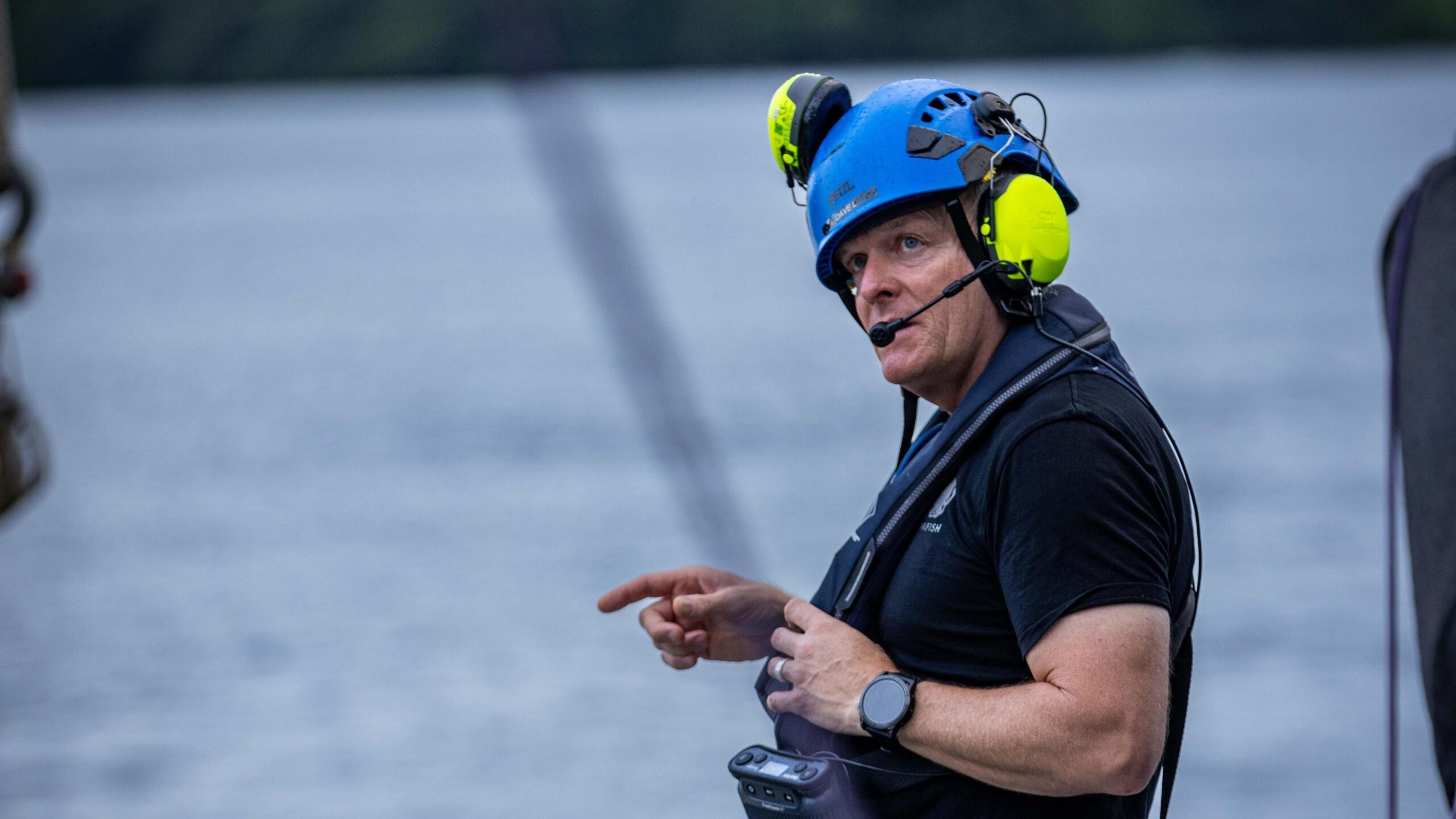 David Lochridge onboard the deck of a ship. He is wearing a headset and helmet - the sea in the background.  