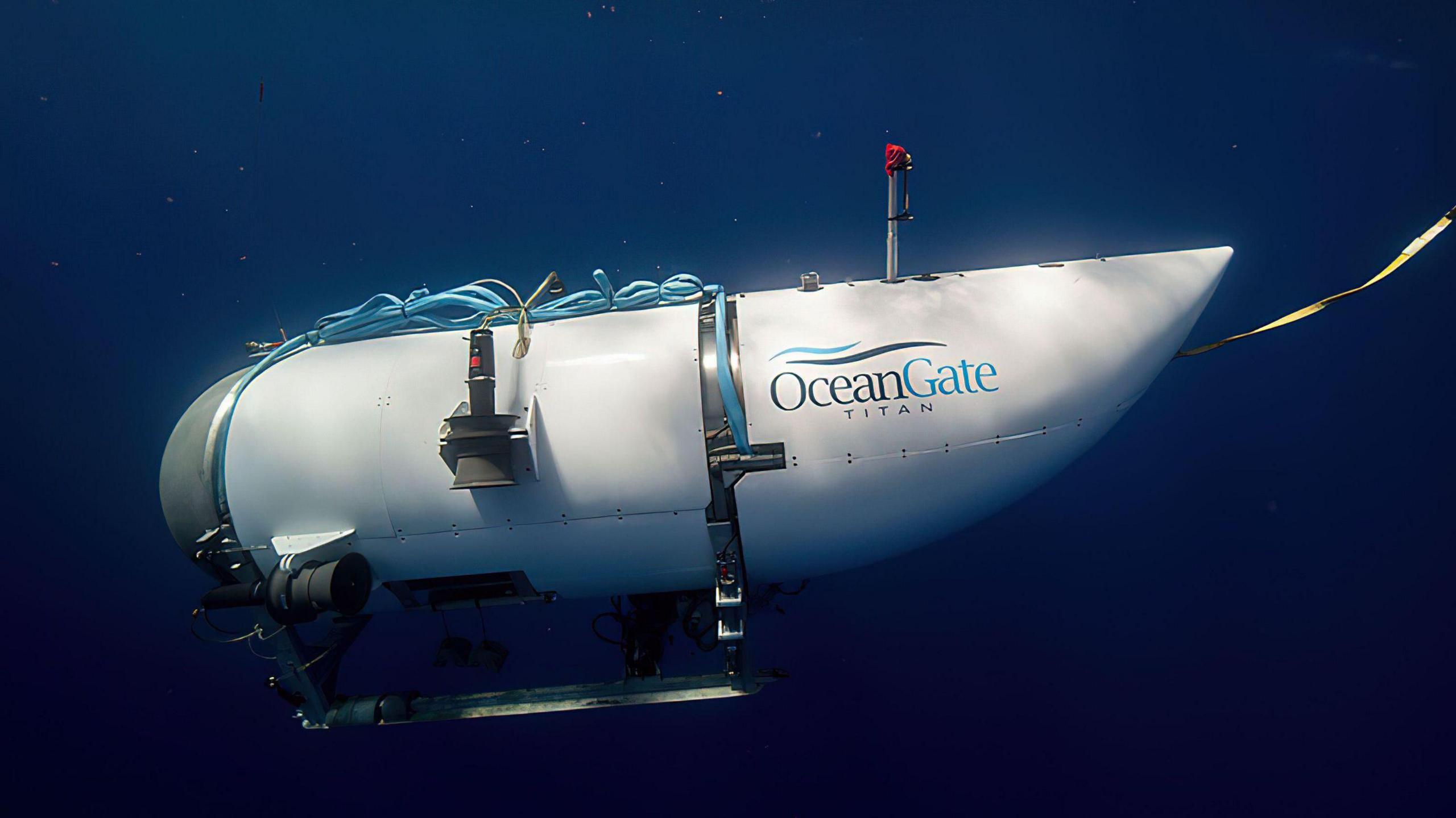 Titan submersible during a dive in the sea. The sub is white with a dome at the front and a tail cover at the back with Oceangate Titan written on its side.  