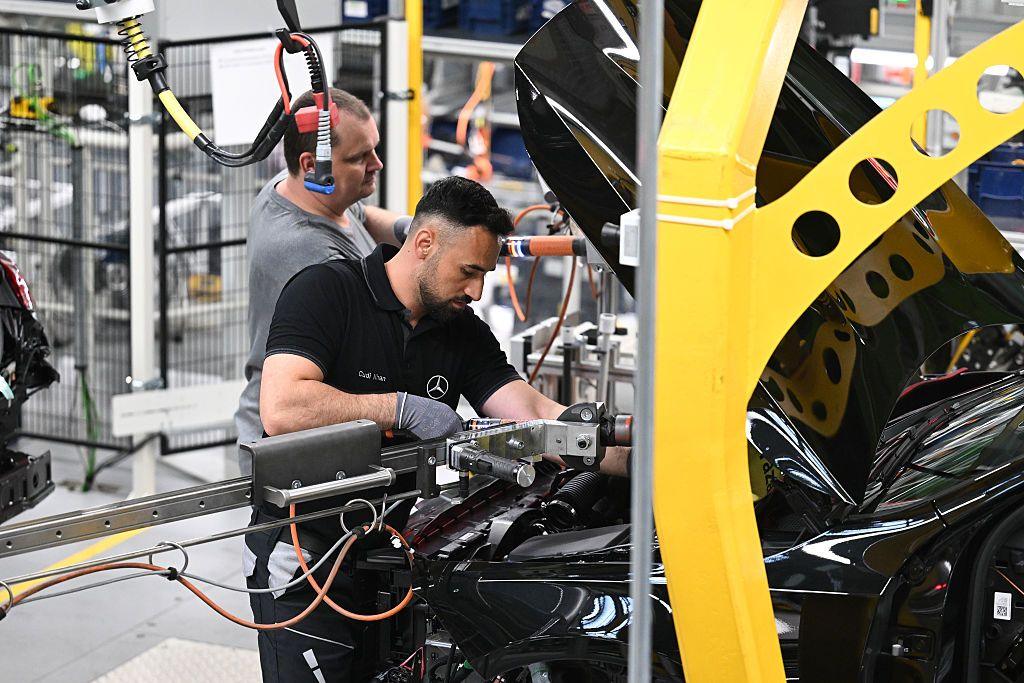 A factory worker peers under the bonnet of a black car and holds a mechanical arm in place as he works