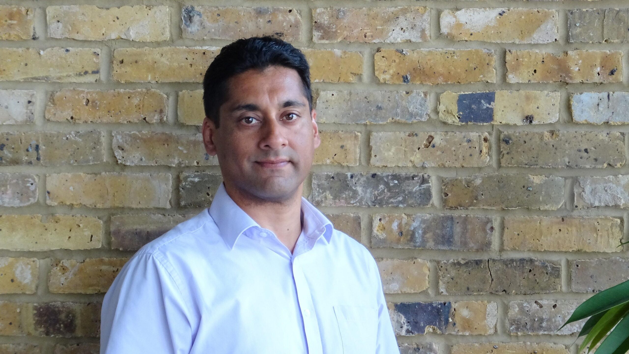 Raman Chagger wearning a white shirt stands against a brick wall